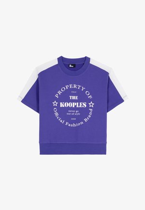 Maglietta corta viola con strisce bianche sulle spalle e testo circolare bianco che recita "PROPRIETÀ DELLA KOOPLES Official Fashion Brand" sul davanti.