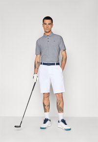Conjunto de golfe masculino com uma camisola polo cinza, calções brancos e acentos azuis. Inclui luvas e um taco de golfe, com tatuagens padronizadas visíveis.