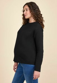 Maglietta nera a maniche lunghe in una vestibilità rilassata con scollatura rotonda. Realizzata in tessuto morbido, abbinata a jeans in denim blu.