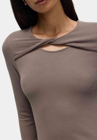 Langdurige ribgebreide top in taupe met een gedraaide detail bij de halslijn en een afgeronde zoom, gemaakt van een zachte, gestructureerde stof.