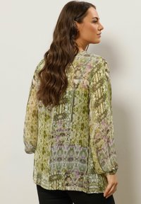 Durchsichtige Bluse mit langen Ärmeln im grünen und lavendelfarbenen Blumenmuster, mit lockerer Passform und elastischen Manschetten, sowie einem abgerundeten Saum.