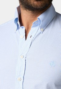 Camicia a righe blu chiaro e bianca, con colletto classico, maniche corte e un sottile logo ricamato sul petto.