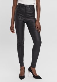 Zwarte high-waisted faux leather broek met een slim fit, vijf zakken en gedetailleerd stikwerk, gecombineerd met zwarte puntige hakken.