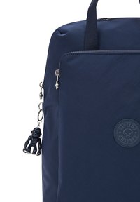 Zaino sintetico blu navy con finitura texturizzata, maniglie superiori e chiusura con zip. Presenta un ciondolo a forma di scimmia e un'etichetta con logo.