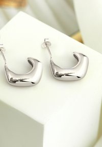 Silverfärgade hoops örhängen med en polerad, böjd design. Slät yta och reflekterande yta, som säkras med en postback.