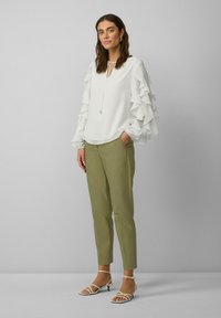 Witte blouse met gerimpelde mouwen, keyhole-halslijn, gecombineerd met olijfgroene op maat gemaakte broek en witte gekruiste sandalen met lage hakken.