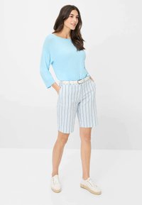 Haut à manches longues bleu clair associé à un short rayé blanc et bleu. Une ceinture blanche et des baskets blanches décontractées complètent la tenue.