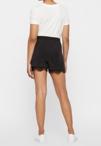 Shorts noirs avec un ourlet en dentelle, dotés d'une taille élastique. Portés avec un t-shirt blanc et des baskets blanches.