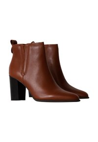 Botas de tobillo de cuero marrón con punta afilada, tirador y tacón grueso negro. Textura suave con detalles de costura mínimos.