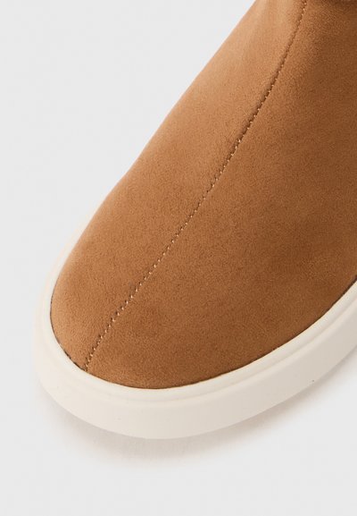 Braune Wildleder-Ankle-Boots mit glatter Oberfläche, runder Zehenpartie und kontrastierendem weißen Gummisohle. Mit sauberem Ziernähten im oberen Bereich.