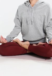 Gray fleece hoodie with a front zipper, worn by a person seated cross-legged on a light purple mat, paired with maroon leggings.