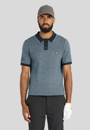 Mand iført en grå perforeret kasket, blå mønstret poloshirt, sorte bukser og en hvid golfhandske på venstre hånd mod en ensfarvet baggrund.