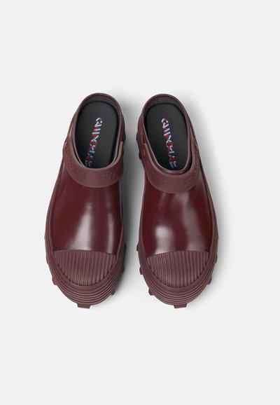 Bordeauxfarbene Clogs mit einer glatten, glänzenden Oberfläche. Gerippte Sohle und Riemen mit Logodetail. Abgerundete Zehenform und offener Rücken für einfaches Anziehen.