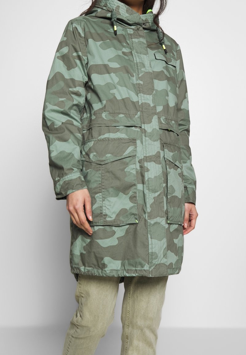 Green camouflage parka with hood, drawstrings, and two large front pockets; made of lightweight fabric with a water-resistant texture.