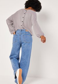 Blusa grigia a coste con chiusura a bottone sul retro, abbinata a jeans a gamba larga di colore azzurro chiaro e sneakers bianche con suola in gomma. Tessuto texture e vestibilità ampia.