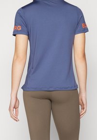 Mörkblå kortärmad pikétröja med orange "BORG"-logga på höger ärm, tillverkad av mjukt, lätt tyg.