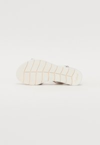 White shoe sole with textured grooves, featuring a light rubber material and subtle accents. Branding visible on the side.