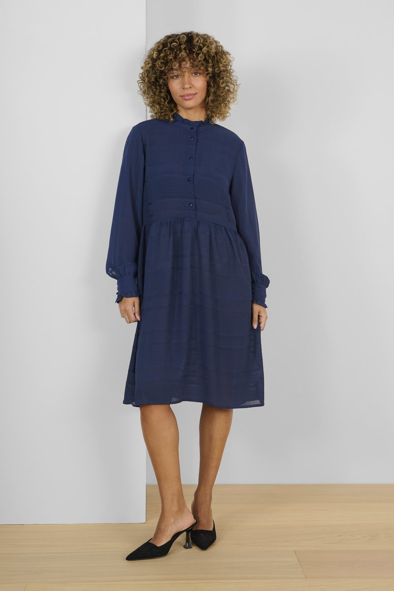 Abito midi blu navy con davanti abbottonato, colletto arricciato, maniche lunghe e sottili righe testurizzate. Un paio di mules con tacco neri.