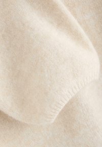 Nærbillede af en beige strikket sweater, der viser blødt, tekstureret uldstof, ribbede manchetter og en glat overflade med en let glans.