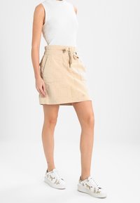 Falda beige con estampado y cintura con cordón, combinada con una blusa sin mangas blanca y zapatillas blancas con diseños de animales.