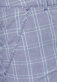 Laivastonsininen ja vaaleansininen ruudullinen kangas, jossa on teksturoitu kudonta, muotoiltu malli ja hienovarainen taskuyksityiskohta.