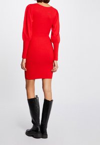 Robe rouge en maille côtelée avec manches longues bouffantes et corsage ajusté, associée à des bottes en cuir noires montantes jusqu'aux genoux. Texture lisse et forme ajustée.