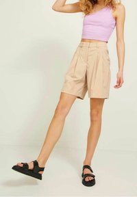 Béžové plisované šortky s vysokým pasem a záhybem, doplněné levandulovým žebrovaným crop topem a černými sandály na pásky.