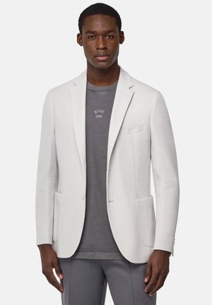 Blazer gris claro en tejido texturizado con solapas con muesca, dos bolsillos frontales y un cierre de un solo botón, llevado sobre una camisa gris oscuro.
