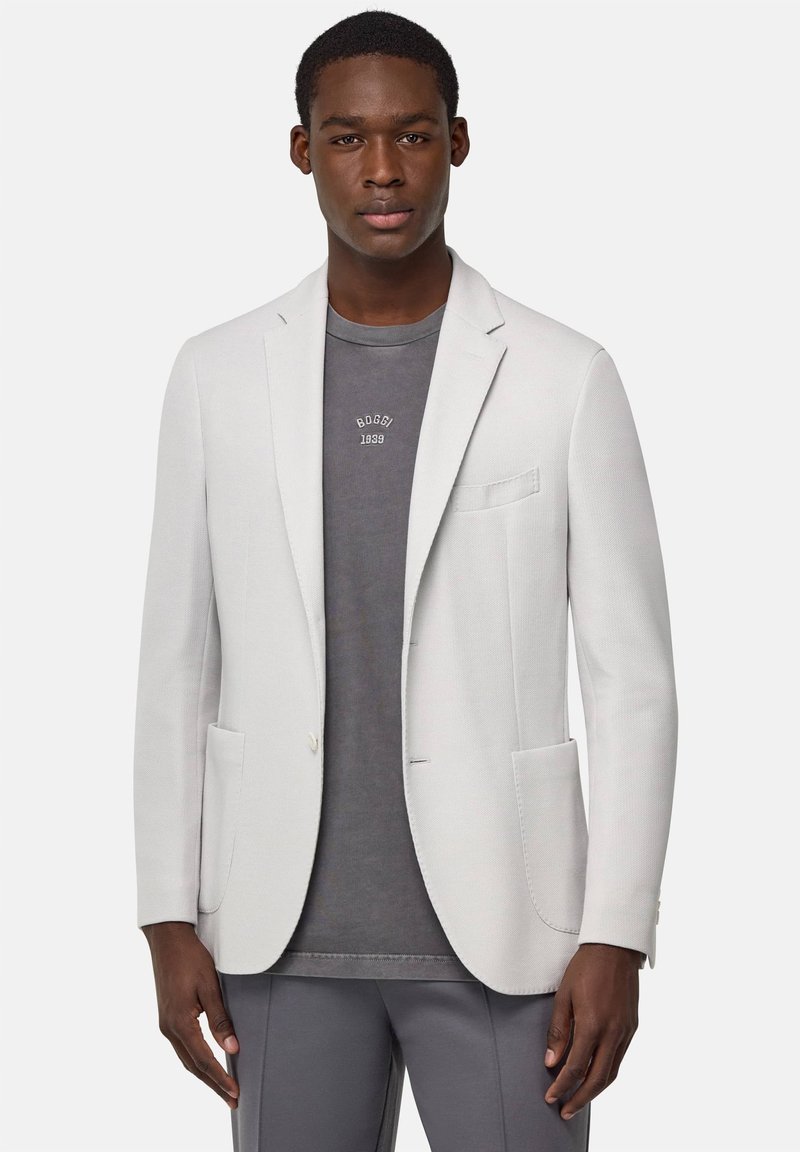 Blazer grigio chiaro in tessuto strutturato con rever a punta, due tasche frontali e chiusura a un bottone, indossato sopra una camicia grigio scuro.