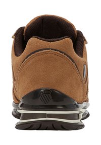 Hnědé semišové sportovní boty s polstrovaným límcem, černým plastovým podpatkem a bílými pruhy na podrážce. Mají texturovaný povrch a detail loga.