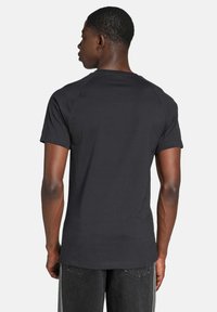 Čierne bavlnené tričko s krátkymi rukávmi, okrúhlym výstrihom a priliehavým strihom na chrbte. Hladká textúra a jednoduchý, nezdobený štýl.