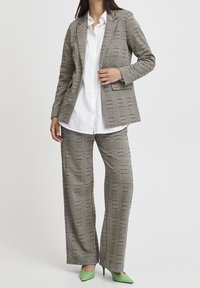 Rutigt blazer i grått och vitt med strukturerad design, parat med vida rutiga byxor. Vit skjorta under och gröna spetsiga klackar.