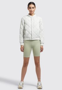 Light quilted bomber jacket in white, featuring diamond patterns, a stand collar, and elastic cuffs, paired with light green bike shorts.
