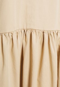 Tejido beige claro con detalles fruncidos en el dobladillo, con una textura suave y un sutil patrón de tejido diagonal.