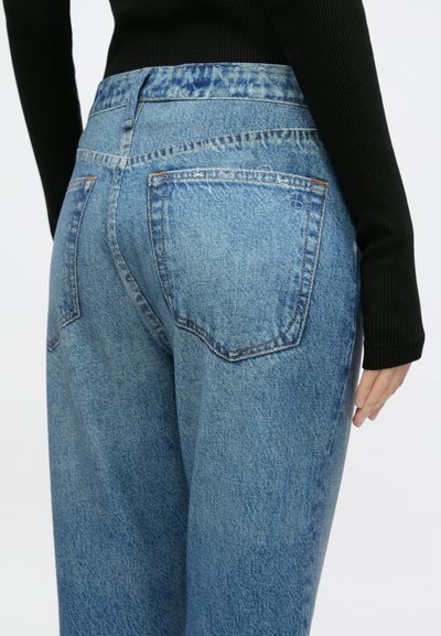 Calças de ganga azul claro com cintura alta, com dois bolsos traseiros e costuras em contraste. Tecido texturizado com um acabamento suave.