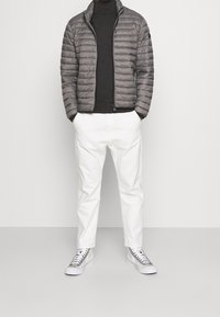 Szara pikowana kurtka, ciemny golf, białe zwężane spodnie i szaro-białe sneakersy. Gładka tekstura, sportowy design i bezszwowe akcenty.