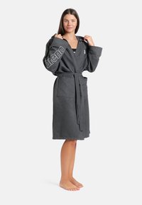 Šedý župan vyrobený z měkké, texturované látky s kapucí, opaskem v pase, dvěma předními kapsami a nápisem "arena" tištěným na rukávu.