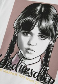 Vit T-shirt med en grafisk design av en tjej med flätor, svart och grå illustration, och text nedanför i svart och guld.