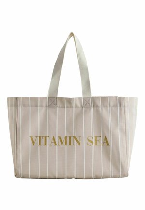 Beige Tragetasche mit dünnen weißen vertikalen Streifen und cremefarbenen Griffen, auf der Vorderseite mit goldenem Text „VITAMIN SEA“.