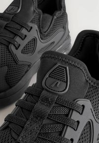 Svarta sportskor med övre del i mesh och gummiinlägg. Funktioner inkluderar tjocka snören, vadderad krage och strukturerade överlayer.