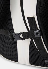 Mochila em preto e branco com tecido em malha, alças ajustáveis e uma fivela de plástico. O contraste de texturas é notável com os painéis suaves.