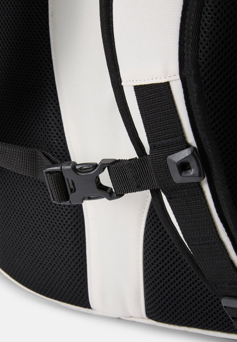 Black and white backpack with mesh fabric, adjustable straps, and a plastic buckle. Notable texture contrasts with smooth paneling.