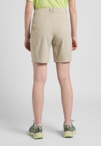 Beige Shorts mit glatter Textur, mittelhohem Bund und geradem Schnitt. Kombiniert mit grünen Wanderschuhen mit strukturierten Gummisohlen.