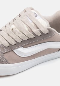Beige canvas sneakers med grå semsket detaljer, hvit side stripe og kremfargede lisser. Har en strukturert hvit gummisåle.