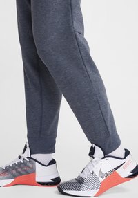 Pantalones deportivos gris oscuro con dobladillos ajustados combinados con zapatillas deportivas blancas, negras y rojas que presentan un upper texturizado y un diseño patternado.