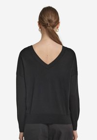 Svart oversized tröja med djup V-ringning, långa ärmar och ribbad fåll. Mjuk textur, minimalistisk design och inga synliga mönster eller detaljer.