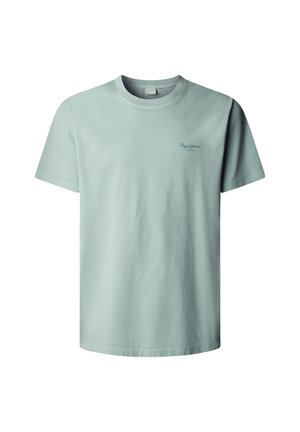 Ung mand med krøllet hår iført en lyseblå t-shirt, lyseblå jeans, brun bælte og brune sko, siddende på en sort skammel.