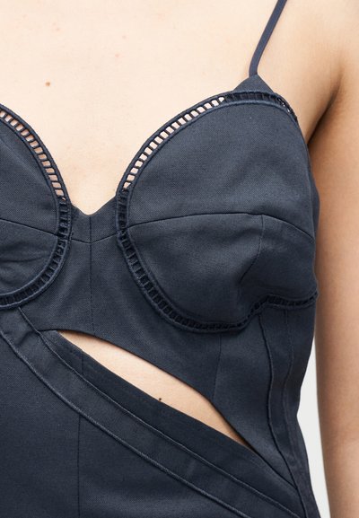 Μαύρο τοπ bustier με υφή, με άνοιγμα κάτω από τις μπανέλες και λεπτές τιράντες, φορεμένο σε γυμνό δέρμα.