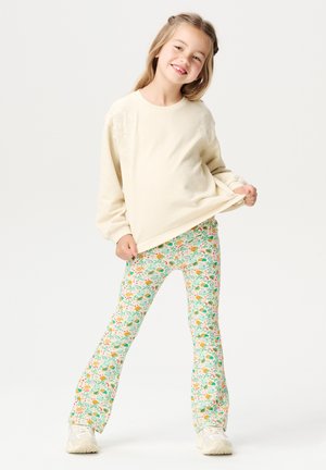 Jasno beżowy sweatshirt z haftem kwiatowym na ramionach, w połączeniu z jasnozielonymi legginsami w wzory z wielokolorowymi kwiatami.