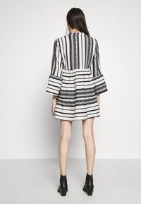 Klänning i svart och vitt med randigt mönster, utsvängd ärmdesign, gathered midja och knälång fåll. Har strukturerade mönster längs med ränderna.